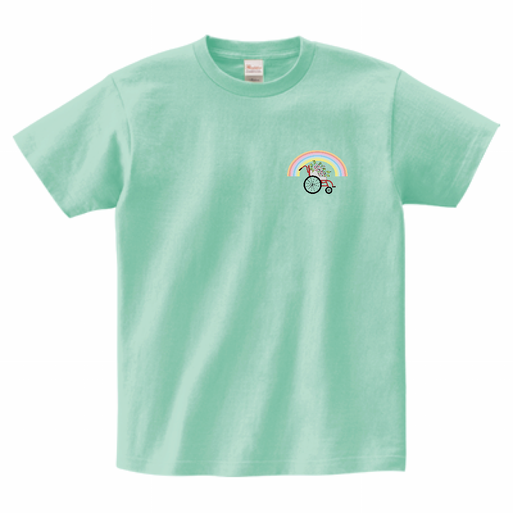 左胸に車いすに花が乗りアーチ状の虹がかかったカラフルなイラストがプリントされたTシャツ。色は薄い緑色。